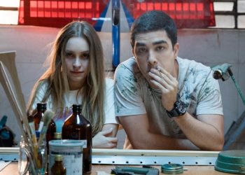 A dupla de filmes A Menina Que Matou Os Pais e O Menino Que Matou Meus Pais retratam a mesma história em duas versões sobre um dos crimes reais que chocou o Brasil no início da década de 2000, a história da família Von Richthofen, em que a filha Suzane Von Richthofen arquitetou o assassinato dos pais Manfred e Marísia von Richthofen junto com o namorado Daniel e o irmão Christian Cravinhos. Caso seja um grande fã de séries e filmes true crime, estes filmes irão saltar aos olhos imediatamente. Mas não espere um retrato fidedigno da história real, pois a frustração pode ser grande. A trama traz apenas um recorte específico deste crime baseado nos depoimentos questionáveis dos condenados que, por sinal, foram descartados pela Lei na época do julgamento, após suas versões serem desconstruídas. Os filmes são interessantes? Sim! As atuações ficam a desejar? Não! Houve uma ousadia em trazer longas semelhantes, aterrados a mesma trama apenas para apresentar visões diferentes da mesma situação. Mas também, era possível construir um único filme com as duas visões contrapostas para criar um conflito maior na trama, o que tornaria interessante e curioso. Quem não conhece os detalhes sobre o caso ou tenha certa preguiça de pesquisar, talvez estes dois filmes sejam um desserviço em que as pessoas podem comprar essas versões ou uma das como verdade absoluta. Por isso, sugiro que vocês assistam aos longas, mas não comprem essas versões e pesquisem sobre o caso real. Narrativa A Menina Que Matou Os Pais e O Menino Que Matou Meus Pais tem como fonte de informação e inspiração os autos do processo do caso, em especial as versões constantes nos depoimentos dos próprios condenados pelos crimes de homicídio, no caso, a Suzane e o Daniel. Os dois filmes apresentam a mesma estrutura narrativa em que ambos iniciam com a mesma sequência (da polícia chegando ao local do crime) e cenas semelhantes em que os detalhes se modificam de acordo com o ponto de vista do personagem que comanda a narrativa do filme. Assistindo aos dois longas, é possível enxergar que as histórias se complementam, ou seja, uma trama preenche a lacuna da outra trama, como o formato do jogo Tetris, o que é um ponto interessante, na minha opinião. Além disso, os filmes trazem um recorte limitado do crime real, ambientado de 1999 a 2002, em que a narração é realizada em 2006, ano do julgamento, ou seja, as tramas são desenvolvidas desde o primeiro dia que a Suzane e o Daniel se conhecem, transitando por toda construção do relacionamento dos dois, até o fatídico dia do assassinato do casal von Richthofen, ganhando um corte brusco no final em que os filmes não relatam nada à respeito do pós-assassinato e a investigação até chegar nos verdadeiros culpados. A frustração pode começar neste ponto, uma vez que as tramas não abrangem o crime real, trazendo um recorte pequeno em dois filmes sendo que ambas perspectivas poderiam ter sido exploradas em um único filme, abordando conflitos interessantes da história e despertando mais o interesse e a indagação do espectador. Ainda assim, os filmes chamam a atenção em como a mesma história ganha moldes diferentes e cínicos pelas perspectivas dos protagonistas, que entregam atuações boas em que as nuances dos personagens mudam drasticamente e de forma positiva. Primeira versão A Menina Que Matou Os Pais é narrada por Daniel que, obviamente se coloca na posição de inocente, pintando a sua figura como a de um garoto apaixonado e manipulado pela namorada rica, com traumas e intenções sombrias que crescem no decorrer da história. Pelo ponto de vista do personagem, temos a perspectiva de um rapaz bom e de boa família, dedicado à profissão do aeromodelismo em que esforça diariamente para juntar dinheiro para sua independência. Por sua visão, o público entende que desde o início do relacionamento, Daniel sempre fora criticado pelos pais de Suzane, que não aceitavam o namoro por conta das diferentes classes sociais e os objetivos de vida, colocando os pais nos papéis de vilões. Os traumas, relatos e o humor oscilante de Suzane e a forma como lida com o autoritarismo dos pais alimentam o lado sombrio de Daniel, que retrata tais circunstâncias como manipulação que mexeram com sua mente, encaminhando-o para o plano maquiavélico da namorada. Segunda versão O Menino Que Matou Meus Pais ganha a narração de Suzane que também cria sua própria versão em que se coloca como a jovem doce e inocente cujo relacionamento abusivo e manipulador a corrompe aos poucos e em pequenos detalhes, como fumar maconha, beber, faltar nas aulas de caratê e na faculdade, além do sufoco crescente de um relacionamento em que Daniel sempre a coloca como culpada quando não podem ficar juntos, alimentando a ideia de que o autoritarismo dos pais atrapalha a vida do casal constantemente. A visão de Suzane apresenta a figura de pais rígidos, mas amorosos, em que a conexão de mãe e filha é mais desenvolvida neste filme. Personagens Mesmo apresentando a mesma estrutura narrativa da mesma história, o ponto alto dos dois filmes são as atuações desenhadas em cada versão que, na minha opinião, apesar de uma ressalva ou outra, não ficam a desejar. A atriz Carla Diaz é a cereja do bolo nos dois filmes em que traz uma performance oscilante e dúbia da personagem. Em A Menina Que Matou Os Pais, vemos uma atuação que traz uma Suzane intensa, densa e sombria, cujo humor ganha nuances drásticas tanto nas cenas mais sexy quanto nas cenas mais maquiavélicas em que ela expõe a impaciência, raiva e seus desejos obscuros, especialmente quando se trata dos pais. Já em O Menino Que Matou Meus Pais, a atriz esbanja cinismo e hipocrisia nas cenas do julgamento em que entrega uma versão sua mais doce e inocente que se desestrutura aos poucos, desmanchando-se até o ápice da submissão e manipulação na relação, lhe anestesiando diante do crime antes e depois de acontecer. O ator Leonardo Bittencourt está bem nos dois filmes e é possível notar o esforço em sua atuação nos dois filmes, mesmo que em algumas cenas a sua performance seja um pouco robótica em certos diálogos e expressões. Seu destaque fica por conta da atuação em O Menino Que Matou Meus Pais, em que vemos um Daniel manipulador e agressivo em uma atmosfera sufocante crescente que ele mesmo cria dentro do relacionamento. No geral, o elenco está bem e ajuda a complementar satisfatoriamente a história, com destaque para os pais de Suzane, Manfred (Leonardo Medeiros) e Marísia (Vera Zimmerman), que entregam boas nuances nas duas versões, enquanto que os pais de Daniel, Nadia (Debora Duboc) e Astrogildo (Augusto Madeira) entregam performances semelhantes nos dois filmes, assim como Andreas (Kauan Ceglio) irmão de Suzane que, por sinal, poderia ter sido desfrutado nas cenas de julgamento em que sua testemunha entraria em conflito com os demais depoimentos. Já o personagem Christian Cravinhos (Allan Souza Lima), sofre uma pequena mudança no final de cada filme, na forma em como age e reage ao ser convidado a participar do assassinato. Considerações finais A Menina Que Matou Os Pais e O Menino Que Matou Meus Pais apresenta a mesma história com a mesma estrutura narrativa em que as cenas ganham detalhes modificados a partir do ponto de vista narrado em suas versões. A trama ganha um recorte limitado do crime real, baseado em depoimentos já desconstruídos, mas com o propósito de focar no desenvolvimento do relacionamento de Suzane e Daniel, em que as atuações são o ponto alto dos filmes, trazendo nuances instigantes de cada personagem, entre uma ressalva e outra. Os dois filmes sobre o caso von Richthofen são interessantes, mas não devem ser considerados como verdade absoluta em momento algum, uma vez que a história real está aí para mostrar as verdadeiras facetas maquiavélicas de Suzane e os irmãos Cravinhos. Os filmes são legais, mas cai no conto quem quer. Ficha Técnica A Menina Que Matou Os Pais/O Menino Que Matou Meus Pais Direção: Mauricio Eça Roteiro: Raphael Montes e Illana Casoy Elenco: Carla Diaz, Leonardo Bittencourt, Vera Zimmerman, Leonardo Medeiros, Debora Duboc, Augusto Madeira, Allan Souza Lima e Kauan Ceglio. Duração: 1h20 cada filme Nota: 7,0