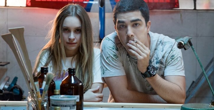 A dupla de filmes A Menina Que Matou Os Pais e O Menino Que Matou Meus Pais retratam a mesma história em duas versões sobre um dos crimes reais que chocou o Brasil no início da década de 2000, a história da família Von Richthofen, em que a filha Suzane Von Richthofen arquitetou o assassinato dos pais Manfred e Marísia von Richthofen junto com o namorado Daniel e o irmão Christian Cravinhos. Caso seja um grande fã de séries e filmes true crime, estes filmes irão saltar aos olhos imediatamente. Mas não espere um retrato fidedigno da história real, pois a frustração pode ser grande. A trama traz apenas um recorte específico deste crime baseado nos depoimentos questionáveis dos condenados que, por sinal, foram descartados pela Lei na época do julgamento, após suas versões serem desconstruídas. Os filmes são interessantes? Sim! As atuações ficam a desejar? Não! Houve uma ousadia em trazer longas semelhantes, aterrados a mesma trama apenas para apresentar visões diferentes da mesma situação. Mas também, era possível construir um único filme com as duas visões contrapostas para criar um conflito maior na trama, o que tornaria interessante e curioso. Quem não conhece os detalhes sobre o caso ou tenha certa preguiça de pesquisar, talvez estes dois filmes sejam um desserviço em que as pessoas podem comprar essas versões ou uma das como verdade absoluta. Por isso, sugiro que vocês assistam aos longas, mas não comprem essas versões e pesquisem sobre o caso real. Narrativa A Menina Que Matou Os Pais e O Menino Que Matou Meus Pais tem como fonte de informação e inspiração os autos do processo do caso, em especial as versões constantes nos depoimentos dos próprios condenados pelos crimes de homicídio, no caso, a Suzane e o Daniel. Os dois filmes apresentam a mesma estrutura narrativa em que ambos iniciam com a mesma sequência (da polícia chegando ao local do crime) e cenas semelhantes em que os detalhes se modificam de acordo com o ponto de vista do personagem que comanda a narrativa do filme. Assistindo aos dois longas, é possível enxergar que as histórias se complementam, ou seja, uma trama preenche a lacuna da outra trama, como o formato do jogo Tetris, o que é um ponto interessante, na minha opinião. Além disso, os filmes trazem um recorte limitado do crime real, ambientado de 1999 a 2002, em que a narração é realizada em 2006, ano do julgamento, ou seja, as tramas são desenvolvidas desde o primeiro dia que a Suzane e o Daniel se conhecem, transitando por toda construção do relacionamento dos dois, até o fatídico dia do assassinato do casal von Richthofen, ganhando um corte brusco no final em que os filmes não relatam nada à respeito do pós-assassinato e a investigação até chegar nos verdadeiros culpados. A frustração pode começar neste ponto, uma vez que as tramas não abrangem o crime real, trazendo um recorte pequeno em dois filmes sendo que ambas perspectivas poderiam ter sido exploradas em um único filme, abordando conflitos interessantes da história e despertando mais o interesse e a indagação do espectador. Ainda assim, os filmes chamam a atenção em como a mesma história ganha moldes diferentes e cínicos pelas perspectivas dos protagonistas, que entregam atuações boas em que as nuances dos personagens mudam drasticamente e de forma positiva. Primeira versão A Menina Que Matou Os Pais é narrada por Daniel que, obviamente se coloca na posição de inocente, pintando a sua figura como a de um garoto apaixonado e manipulado pela namorada rica, com traumas e intenções sombrias que crescem no decorrer da história. Pelo ponto de vista do personagem, temos a perspectiva de um rapaz bom e de boa família, dedicado à profissão do aeromodelismo em que esforça diariamente para juntar dinheiro para sua independência. Por sua visão, o público entende que desde o início do relacionamento, Daniel sempre fora criticado pelos pais de Suzane, que não aceitavam o namoro por conta das diferentes classes sociais e os objetivos de vida, colocando os pais nos papéis de vilões. Os traumas, relatos e o humor oscilante de Suzane e a forma como lida com o autoritarismo dos pais alimentam o lado sombrio de Daniel, que retrata tais circunstâncias como manipulação que mexeram com sua mente, encaminhando-o para o plano maquiavélico da namorada. Segunda versão O Menino Que Matou Meus Pais ganha a narração de Suzane que também cria sua própria versão em que se coloca como a jovem doce e inocente cujo relacionamento abusivo e manipulador a corrompe aos poucos e em pequenos detalhes, como fumar maconha, beber, faltar nas aulas de caratê e na faculdade, além do sufoco crescente de um relacionamento em que Daniel sempre a coloca como culpada quando não podem ficar juntos, alimentando a ideia de que o autoritarismo dos pais atrapalha a vida do casal constantemente. A visão de Suzane apresenta a figura de pais rígidos, mas amorosos, em que a conexão de mãe e filha é mais desenvolvida neste filme. Personagens Mesmo apresentando a mesma estrutura narrativa da mesma história, o ponto alto dos dois filmes são as atuações desenhadas em cada versão que, na minha opinião, apesar de uma ressalva ou outra, não ficam a desejar. A atriz Carla Diaz é a cereja do bolo nos dois filmes em que traz uma performance oscilante e dúbia da personagem. Em A Menina Que Matou Os Pais, vemos uma atuação que traz uma Suzane intensa, densa e sombria, cujo humor ganha nuances drásticas tanto nas cenas mais sexy quanto nas cenas mais maquiavélicas em que ela expõe a impaciência, raiva e seus desejos obscuros, especialmente quando se trata dos pais. Já em O Menino Que Matou Meus Pais, a atriz esbanja cinismo e hipocrisia nas cenas do julgamento em que entrega uma versão sua mais doce e inocente que se desestrutura aos poucos, desmanchando-se até o ápice da submissão e manipulação na relação, lhe anestesiando diante do crime antes e depois de acontecer. O ator Leonardo Bittencourt está bem nos dois filmes e é possível notar o esforço em sua atuação nos dois filmes, mesmo que em algumas cenas a sua performance seja um pouco robótica em certos diálogos e expressões. Seu destaque fica por conta da atuação em O Menino Que Matou Meus Pais, em que vemos um Daniel manipulador e agressivo em uma atmosfera sufocante crescente que ele mesmo cria dentro do relacionamento. No geral, o elenco está bem e ajuda a complementar satisfatoriamente a história, com destaque para os pais de Suzane, Manfred (Leonardo Medeiros) e Marísia (Vera Zimmerman), que entregam boas nuances nas duas versões, enquanto que os pais de Daniel, Nadia (Debora Duboc) e Astrogildo (Augusto Madeira) entregam performances semelhantes nos dois filmes, assim como Andreas (Kauan Ceglio) irmão de Suzane que, por sinal, poderia ter sido desfrutado nas cenas de julgamento em que sua testemunha entraria em conflito com os demais depoimentos. Já o personagem Christian Cravinhos (Allan Souza Lima), sofre uma pequena mudança no final de cada filme, na forma em como age e reage ao ser convidado a participar do assassinato. Considerações finais A Menina Que Matou Os Pais e O Menino Que Matou Meus Pais apresenta a mesma história com a mesma estrutura narrativa em que as cenas ganham detalhes modificados a partir do ponto de vista narrado em suas versões. A trama ganha um recorte limitado do crime real, baseado em depoimentos já desconstruídos, mas com o propósito de focar no desenvolvimento do relacionamento de Suzane e Daniel, em que as atuações são o ponto alto dos filmes, trazendo nuances instigantes de cada personagem, entre uma ressalva e outra. Os dois filmes sobre o caso von Richthofen são interessantes, mas não devem ser considerados como verdade absoluta em momento algum, uma vez que a história real está aí para mostrar as verdadeiras facetas maquiavélicas de Suzane e os irmãos Cravinhos. Os filmes são legais, mas cai no conto quem quer. Ficha Técnica A Menina Que Matou Os Pais/O Menino Que Matou Meus Pais Direção: Mauricio Eça Roteiro: Raphael Montes e Illana Casoy Elenco: Carla Diaz, Leonardo Bittencourt, Vera Zimmerman, Leonardo Medeiros, Debora Duboc, Augusto Madeira, Allan Souza Lima e Kauan Ceglio. Duração: 1h20 cada filme Nota: 7,0